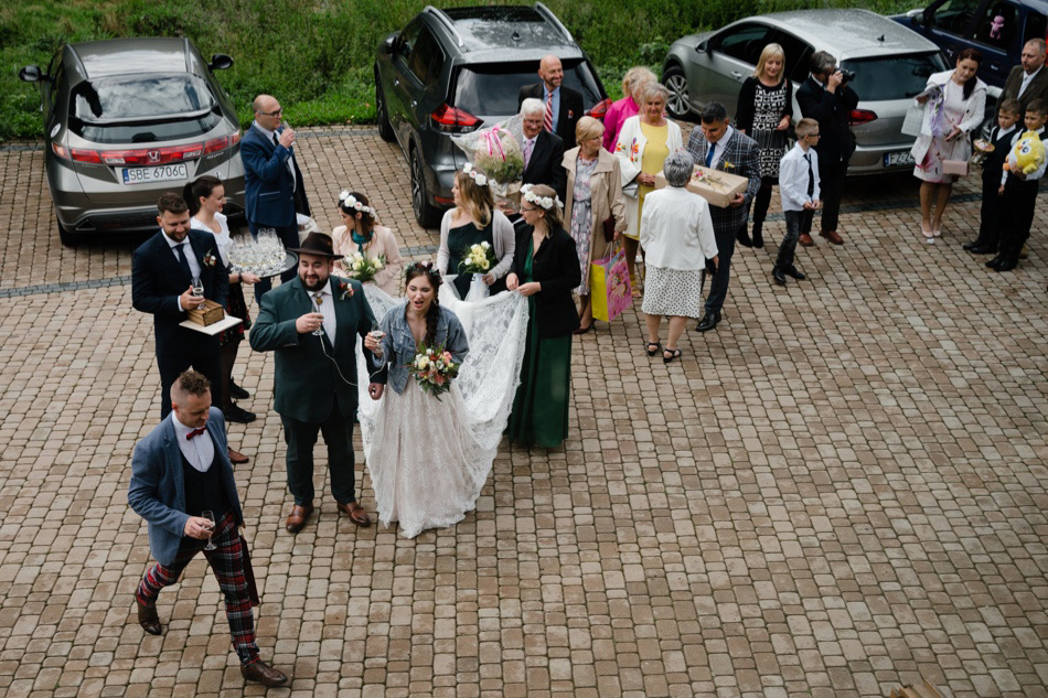 Pani młoda w sukni ślubnej z welonem i trenem podczas toastu przed lokalem weselnym Gościniec Jaworze Nałęże