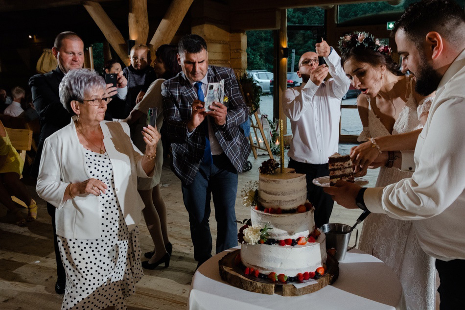 Goście weselni podczas krojenia tortu weselnego przez parę młodą